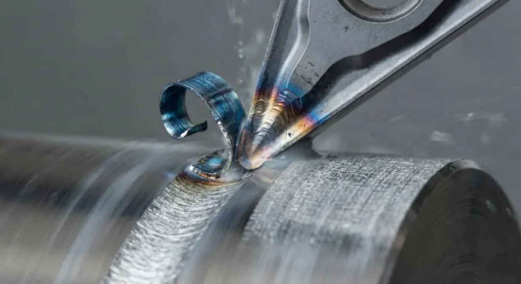 Macro photography of CNC turning insert cutting stainless steel with blue metal chips and coolant.