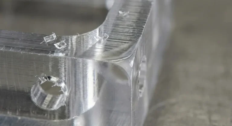 Macro view of milled PMMA surface showing toolpath lines, small chips, and a slight heat smear zone near an edge